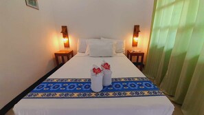 A neatly made bed with white linens, two bedside tables with lamps, and a decorative blue and white patterned runner.