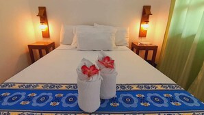 Ein ordentlich bezogenes Bett mit weißen Leinen, zwei Handtücher mit roten Blumen und einer blau gemusterten Tagesdecke.