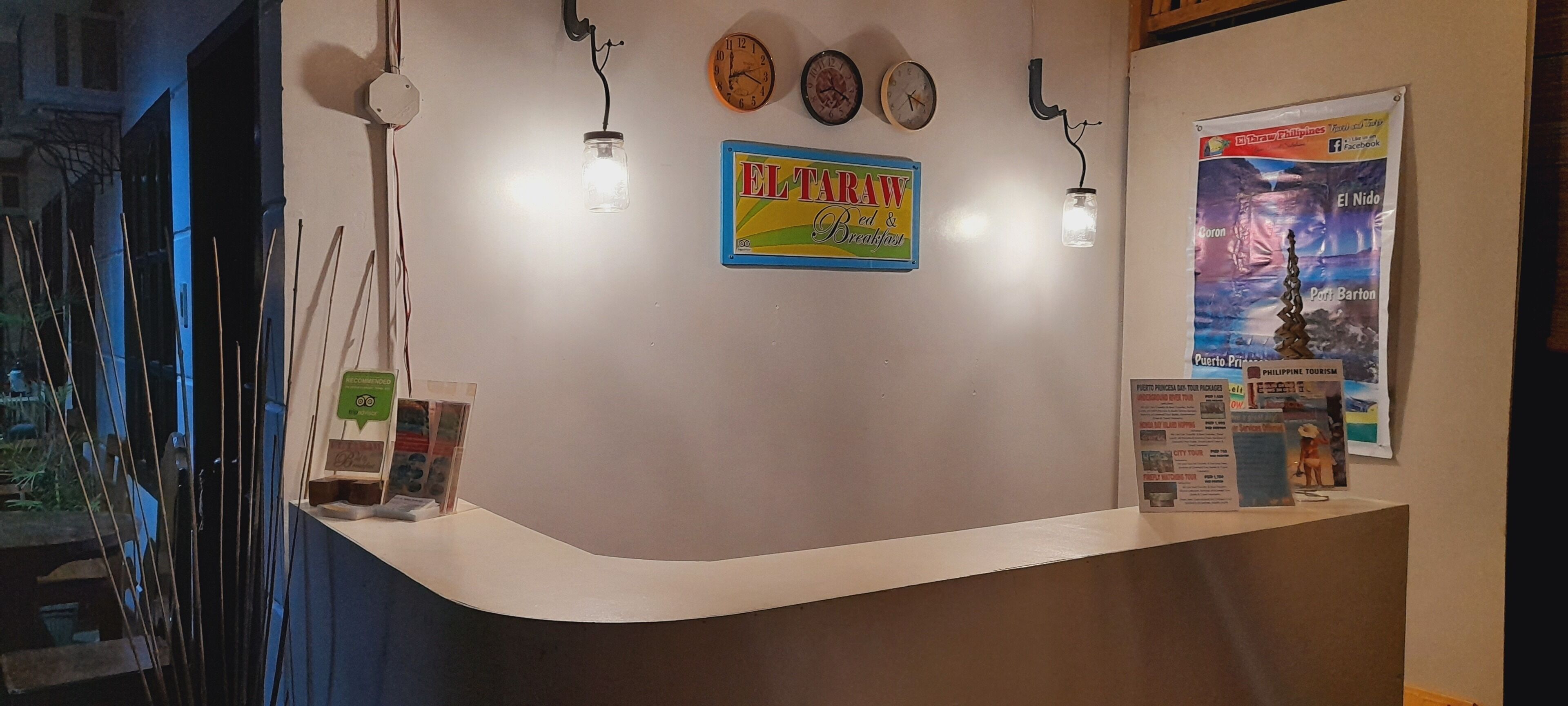 A reception desk with a sign for 'EL TAW Bread & Breakfast', clocks, and a travel poster.