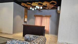A reception area with a wooden reception desk, a patterned sofa, and a ceiling with geometric light fixtures. - Devrana (Khatoli)