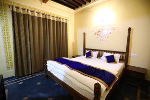 A neatly made bed with a blue and white bedspread, a wooden headboard, and a patterned curtain. - Devrana (Khatoli)