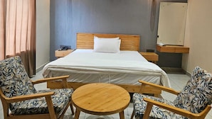 A hotel room with a large bed, two nightstands, a round wooden table, two patterned armchairs, and two wall-mounted light fixtures. - Devrana (Khatoli)