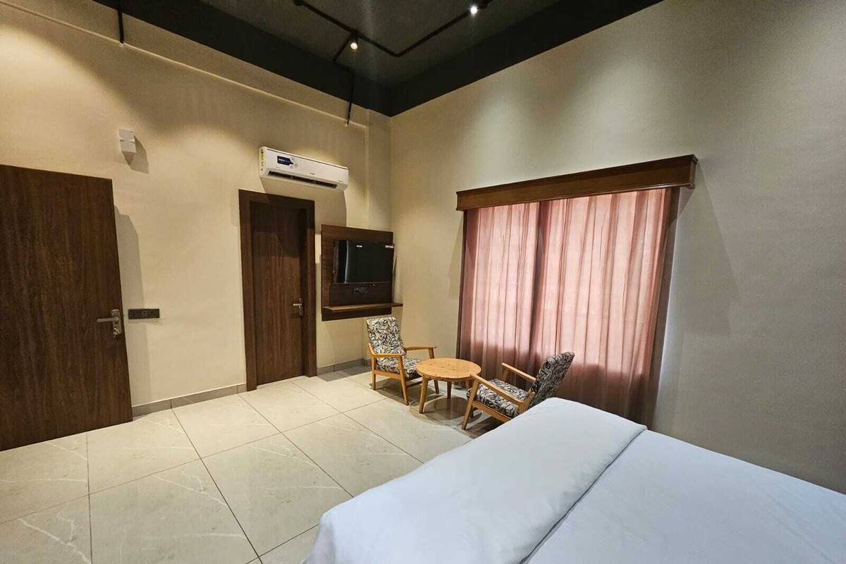 Habitación de hotel con cama, televisión montada en la pared, una mesita con sillas y ventana con cortinas.