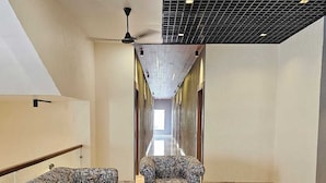 A modern hotel lobby with a long corridor, patterned sofas, a glass coffee table, and a ceiling fan. - Devrana (Khatoli)