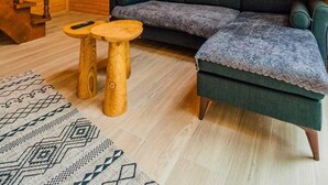 Ein gemütliches Loft-Zimmer mit Holzboden, einem grünen Ecksofa, einem Holztisch und einem gemusterten Teppich.