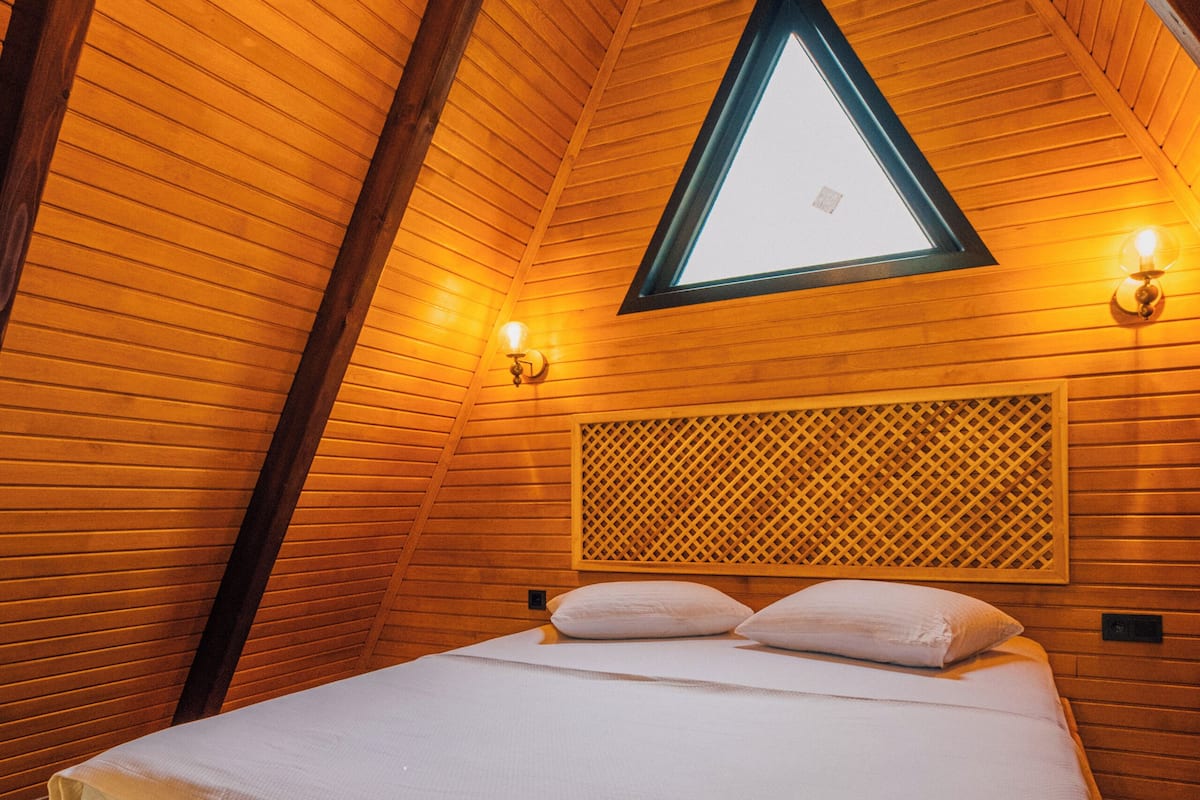Ein Zimmer mit Holzwänden, schrägen Decken, einem Bett mit weißer Bettwäsche und einem Oberlicht.