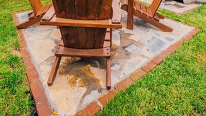 Ein Garten mit einer Steinterrasse, Holz-Adirondack-Stühlen und einem Kamin aus Stein.