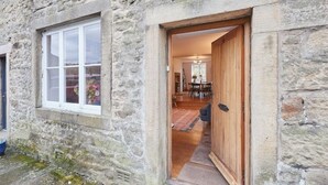A stone building with a wooden door leading to a dining area with a table and chairs. - Stunning 3 bed Yorkshire Dales cottage (Skyreholme)