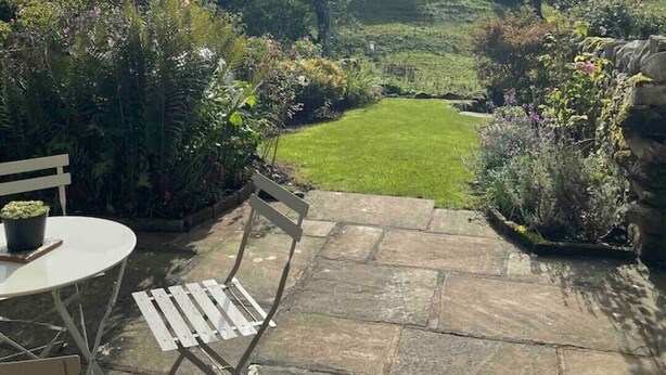 A patio with a table and chairs, a stone pathway, and a view of a green field and distant hills. - Stunning 3 bed Yorkshire Dales cottage (Skyreholme)