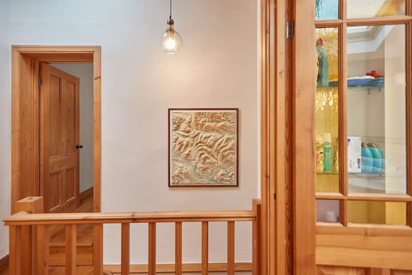 Un escalier en bois avec une rampe, une porte en bois et un luminaire fixé au mur.
