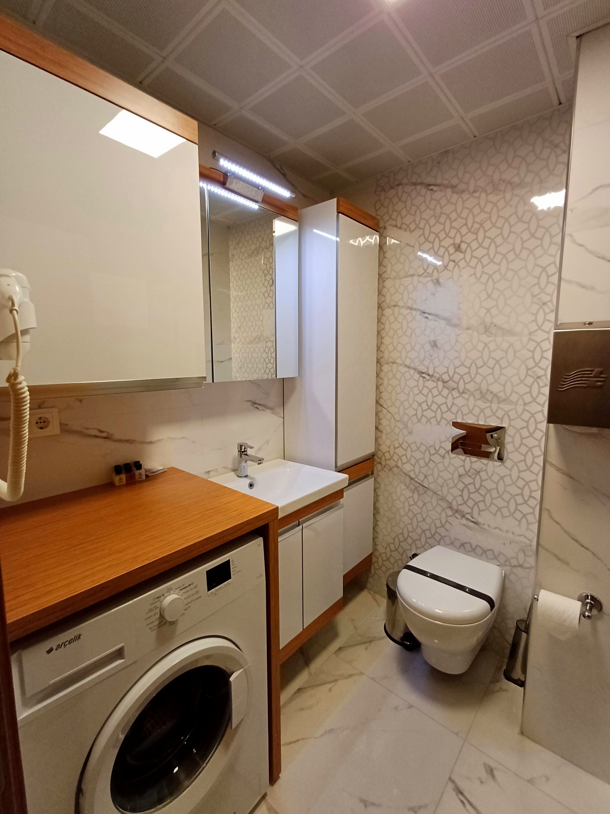 A modern bathroom with a built-in washing machine, a toilet, and a sink with a mirror above it.