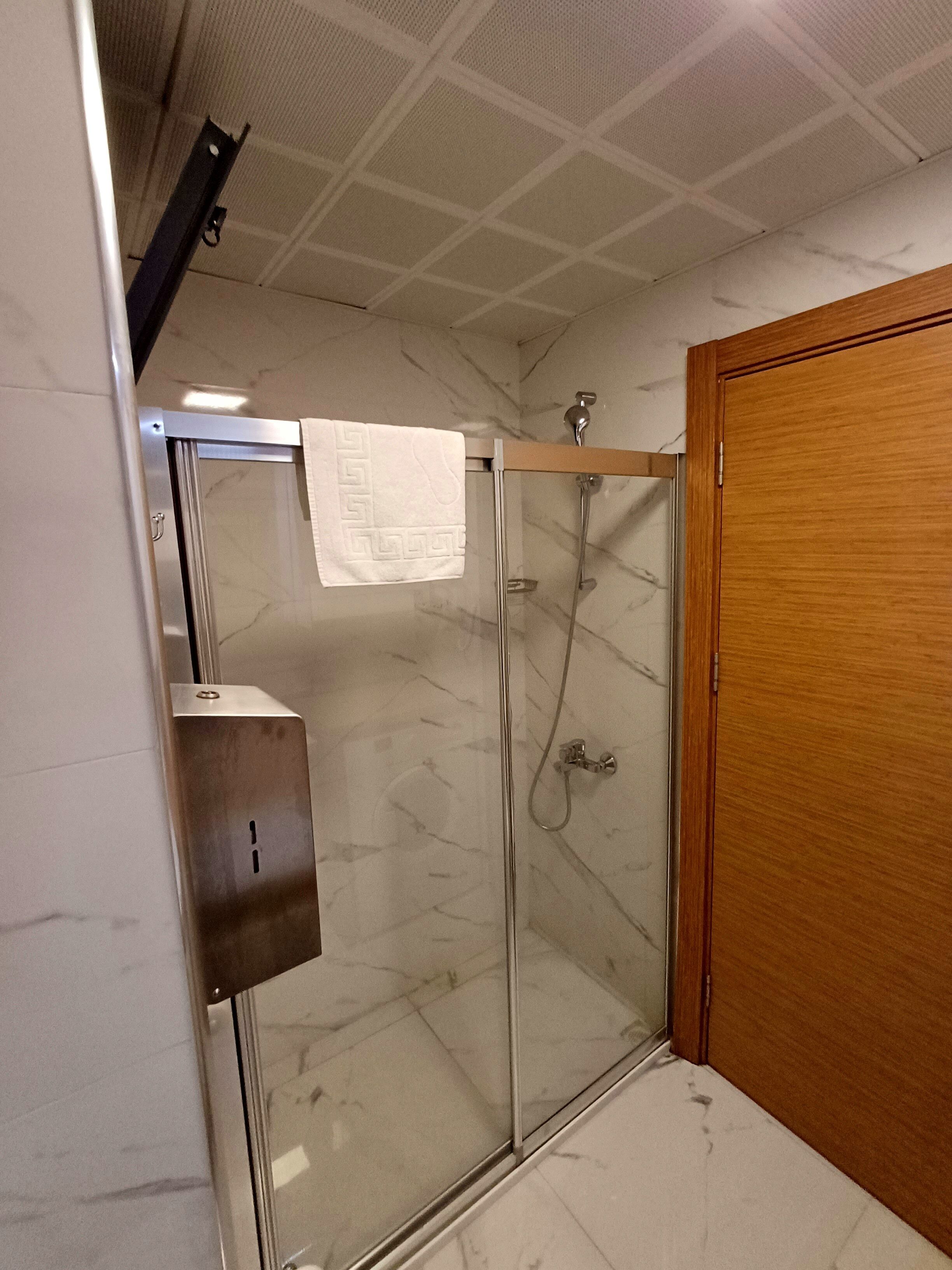 Ducha con paredes de vidrio y puerta de madera, con una toalla colgada en la puerta y un panel de control metálico.