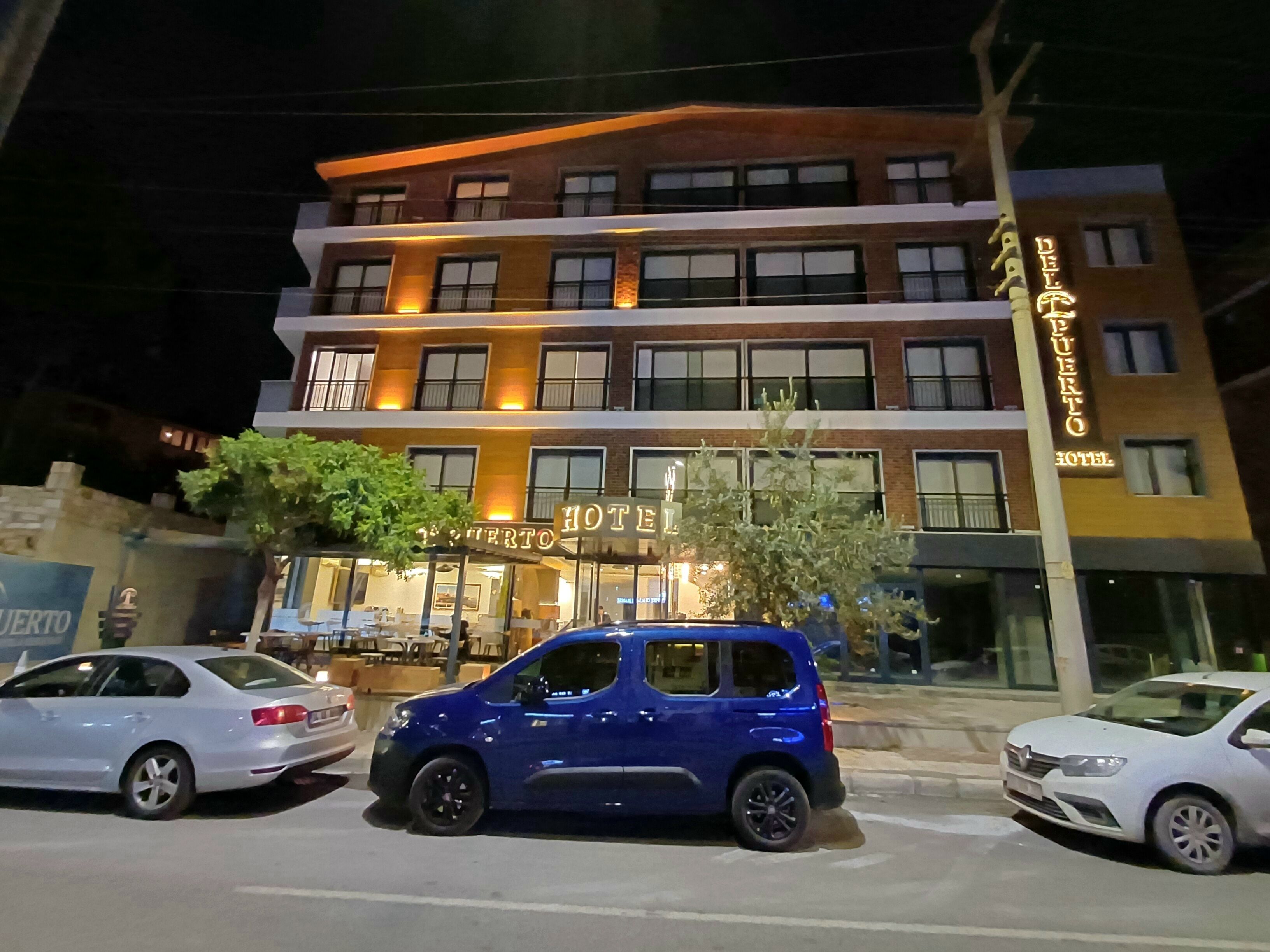 A hotel with a sign reading "HOTEL PUERTO" and a blue car parked in front.