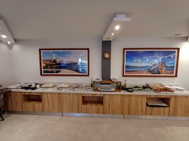 Uma cozinha moderna com armários de madeira, uma ilha integrada com diversos alimentos e duas pinturas emolduradas na parede.