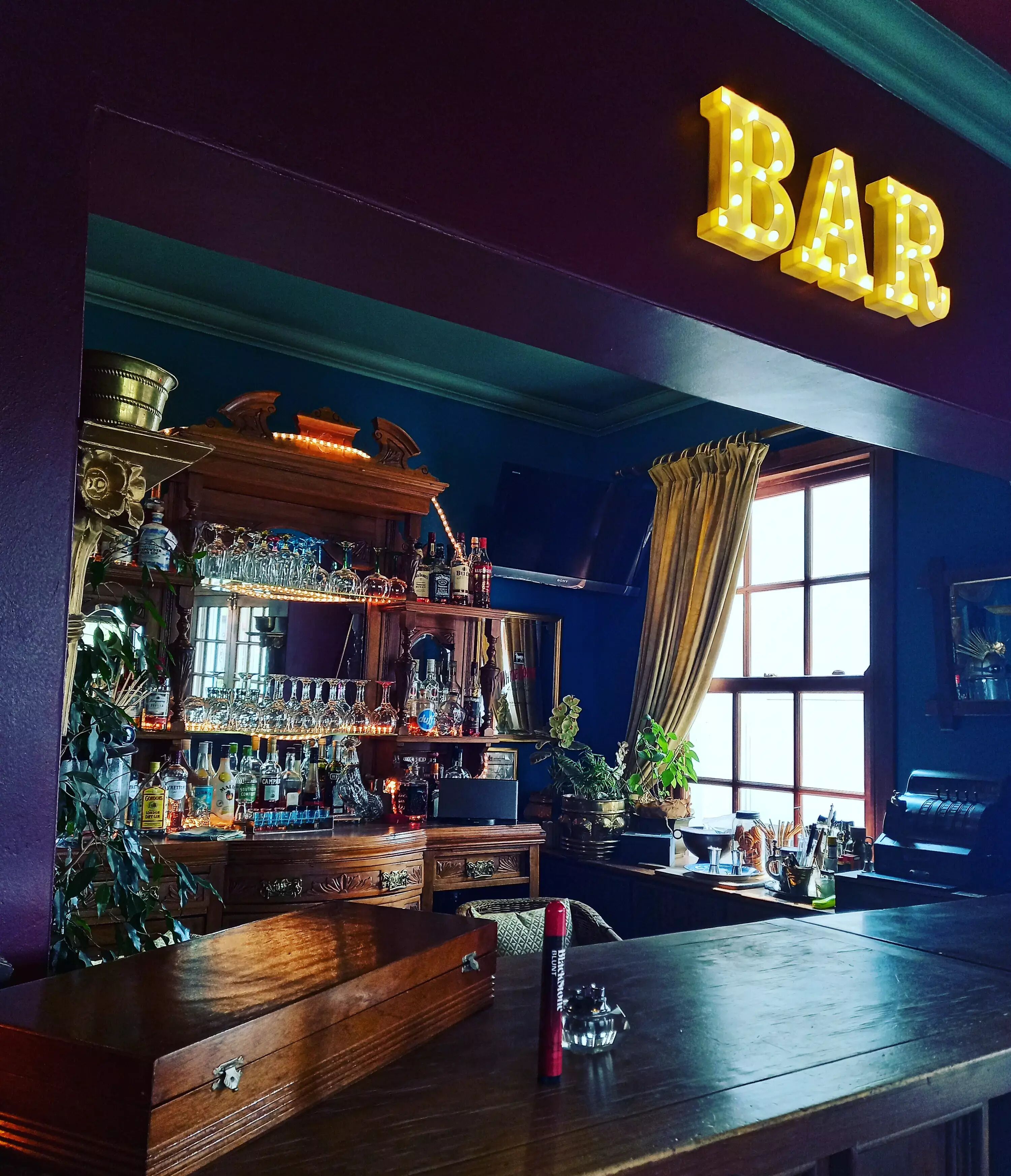 Un bar con un letrero que dice 'BAR', estantes con botellas, vasos y una barra de madera.