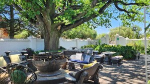 A courtyard with outdoor furniture, a large tree, and a white wall. - Oak View Manor (Lesedi)
