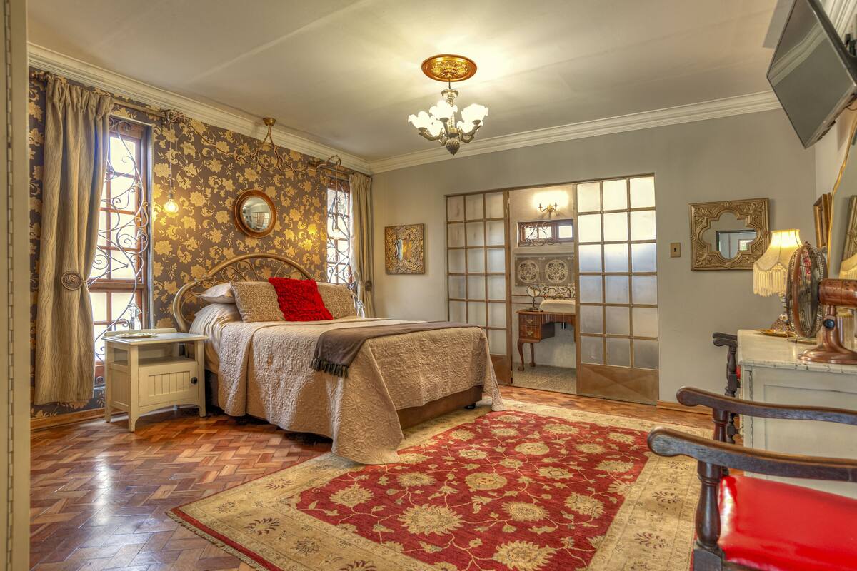 Quarto com cama, mesa de cabeceira, cômoda, espelho e janela com cortinas.