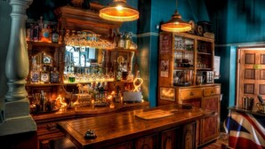 A bar with wooden shelves filled with bottles and glasses, and two hanging lamps. - Oak View Manor (Lesedi)