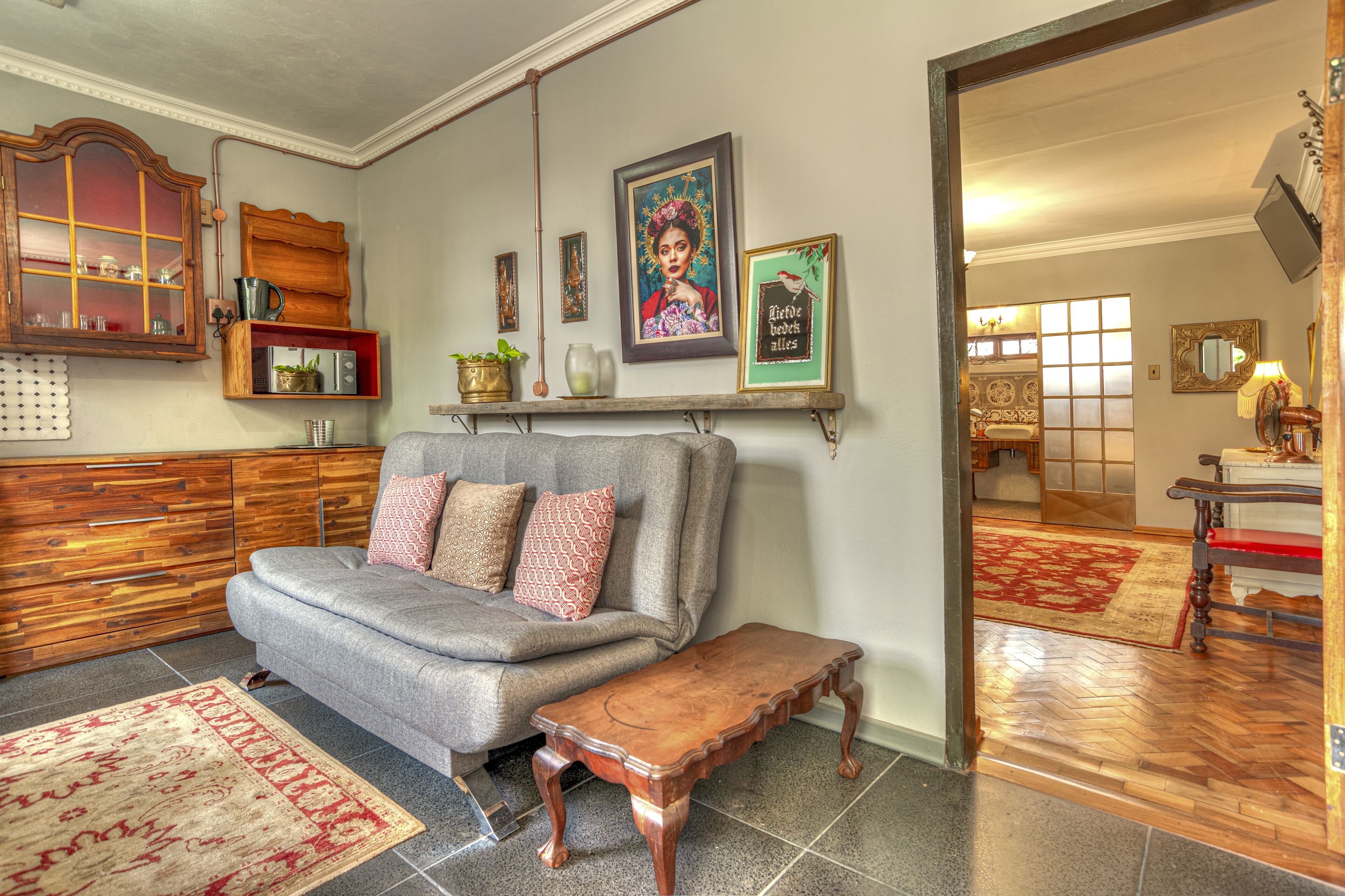 Una sala de estar con un sofá gris, un banco de madera y un tapete rojo. Hay un mueble de madera con puertas de vidrio, una estantería con objetos decorativos y un cuadro en la pared.