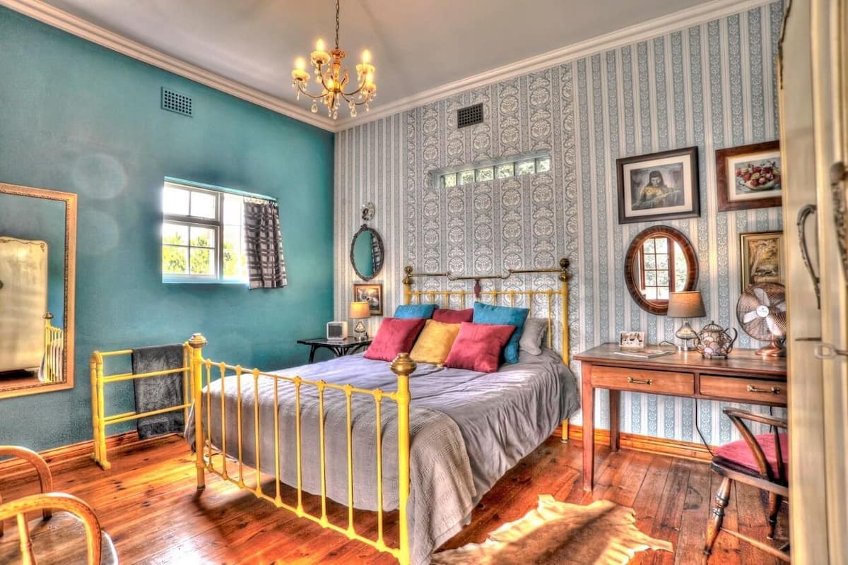 Quarto com cama, escrivaninha, cadeira, espelho e lustre.