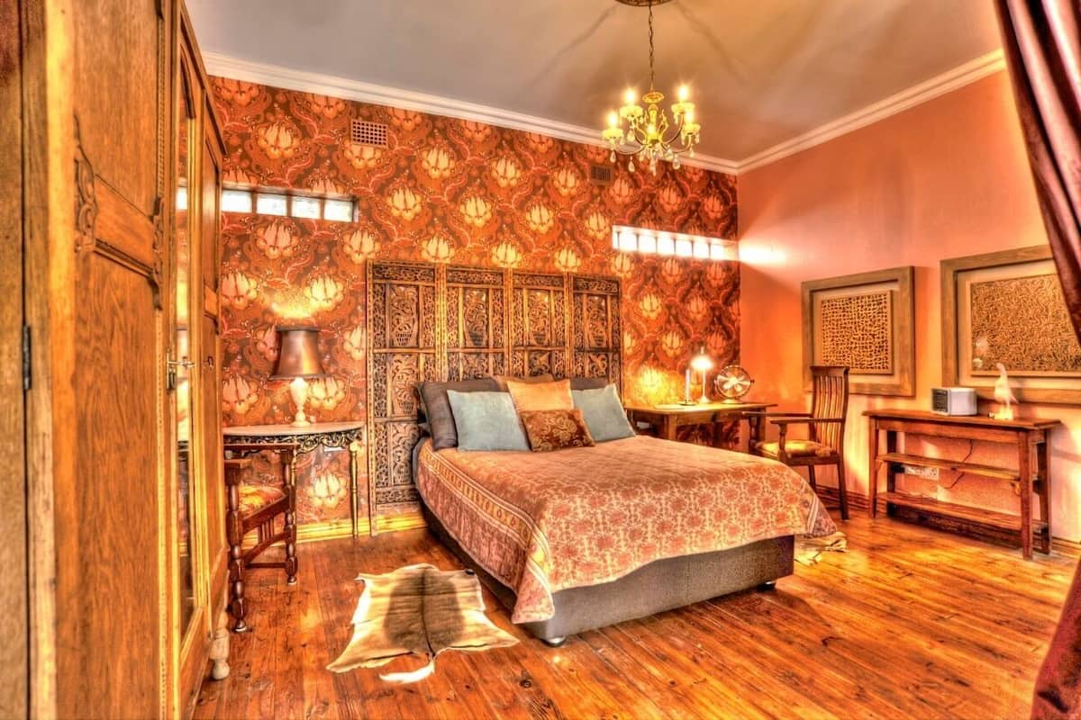 Quarto com cama grande, piso de madeira, papel de parede estampado e um lustre.