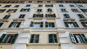 A multi-story building with a central entrance featuring a large barred window, flanked by balconies and multiple windows with green shutters. - Casa Fabrizio (Rome)