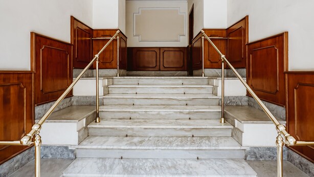 A grand staircase with marble steps and wooden paneling, leading to a landing with a white ceiling and decorative molding. - Casa Fabrizio (Rome)