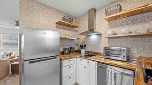 Una cocina compacta con refrigerador de acero inoxidable, tostadora integrada, encimeras de madera y papel tapiz estampado.