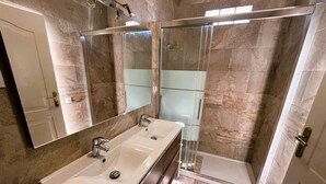 Une salle de bain avec un double vasque, un grand miroir et une douche à l’italienne.