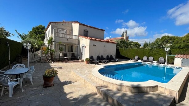 Un espace piscine avec une terrasse en pierre, des sièges d’extérieur et un bâtiment doté d’un toit en tuiles.