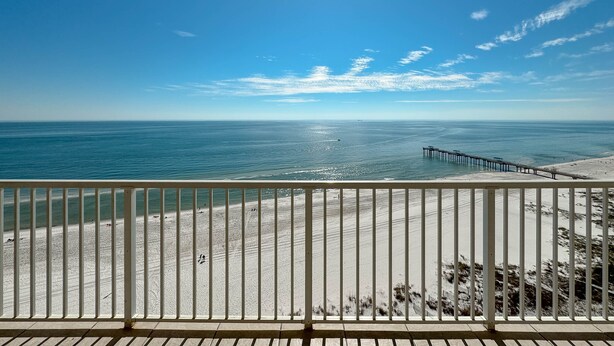 A beach view from a balcony with a white railing, sandy beach, and a pier extending into the ocean. - Admirals Quarters 1403-Beachfront | 2 King Suites | Free parking for 2 Vehicles (Orange Beach)