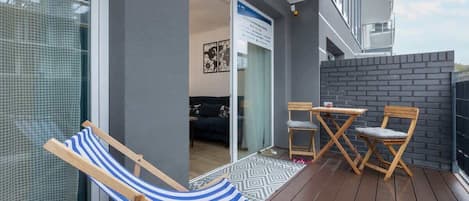 A balcony with a wooden floor, a striped beach chair, and a small table with two chairs.