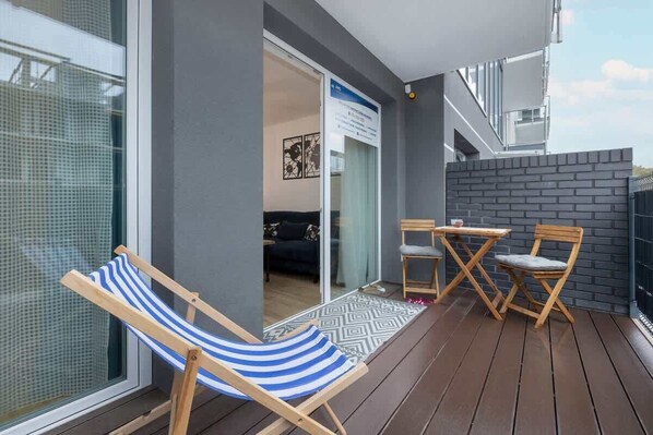 A balcony with a wooden floor, a striped beach chair, and a small table with two chairs.