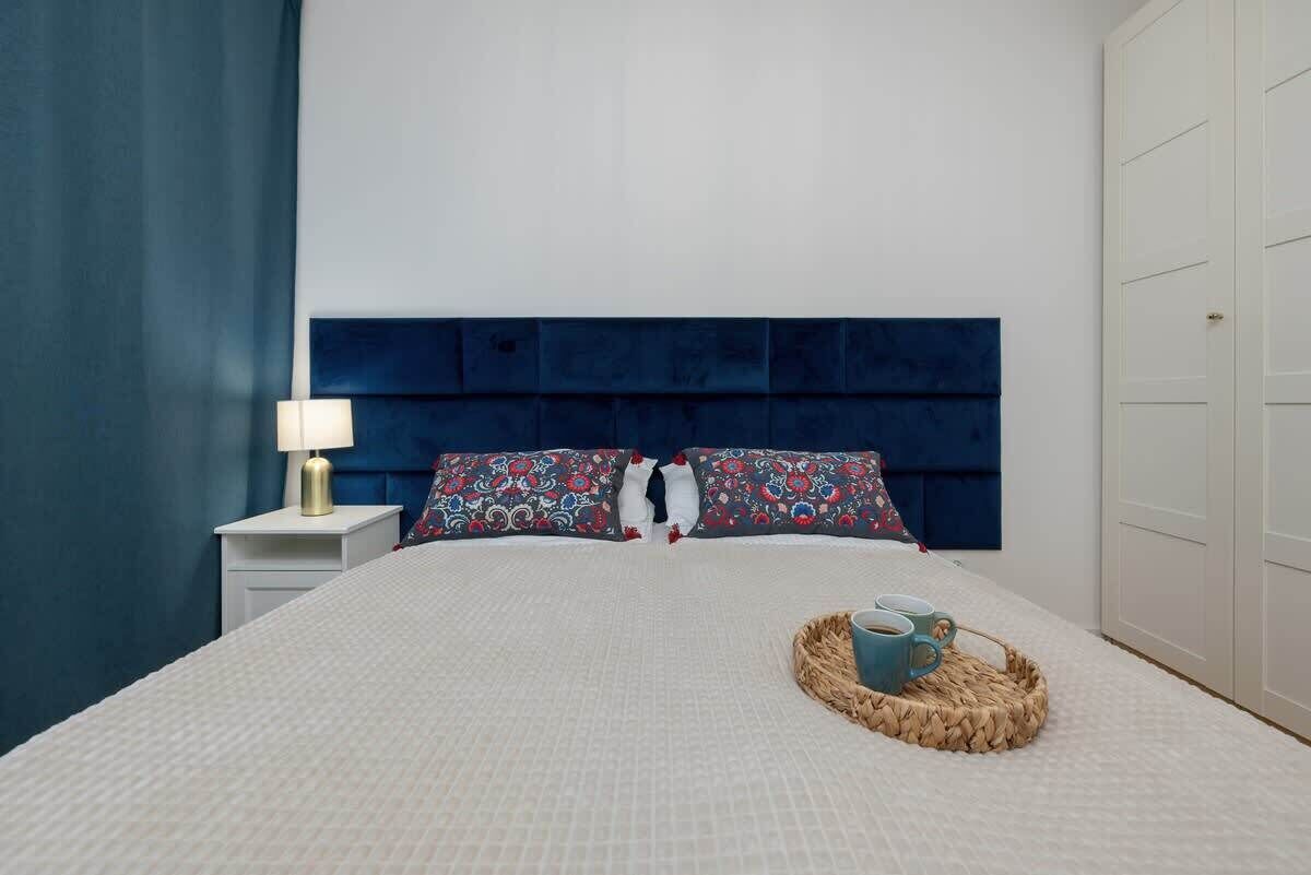 Un letto ben rifatto con cuscini decorati, una lampada da comodino e un vassoio con tazze sul letto.