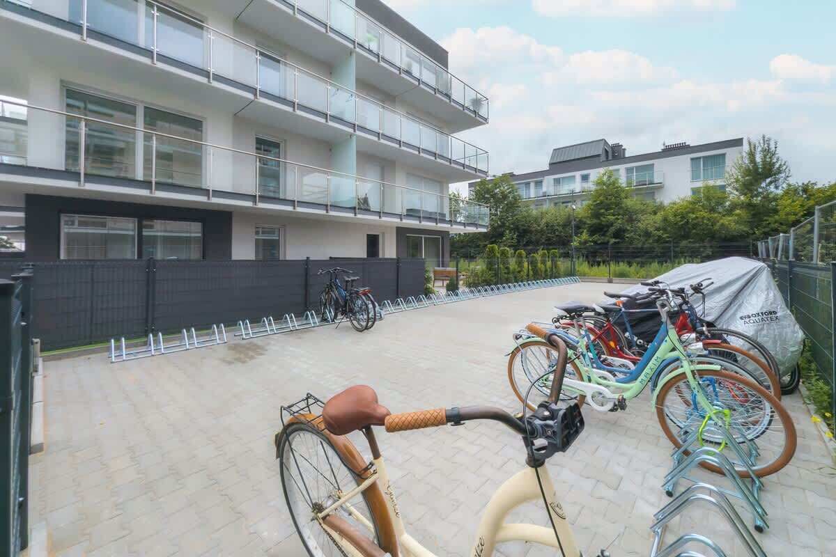 A modern apartment building with multiple balconies, bicycles parked outside, and a paved courtyard.