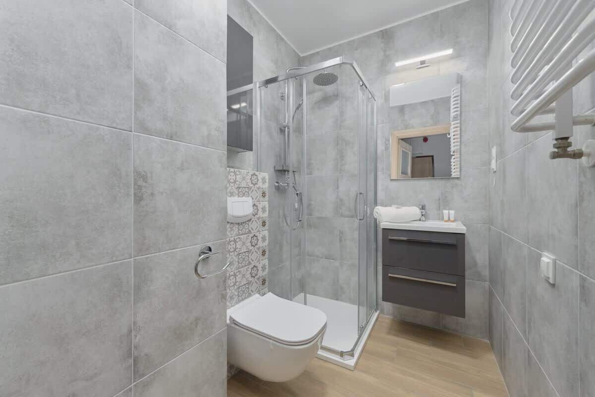 Une salle de bain moderne avec des carreaux gris, une douche à parois de verre, des toilettes et un meuble-lavabo avec un miroir.