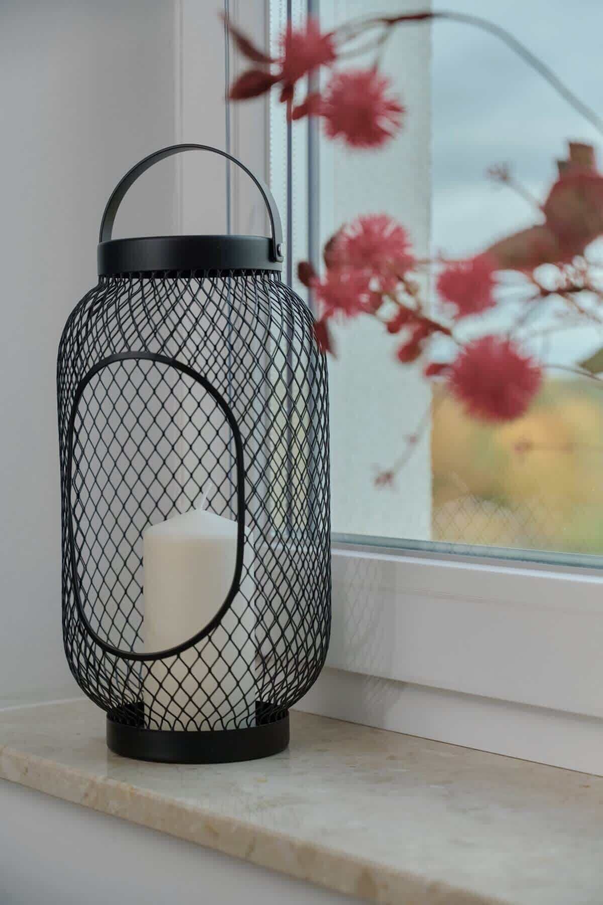 A black metal lantern with a white candle holder on a windowsill.