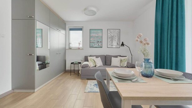 Un salon moderne avec un canapé gris, une table à manger avec des assiettes et un vase, et une fenêtre avec des rideaux.