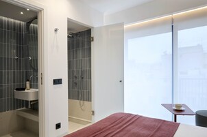 Un baño moderno con ducha, lavabo y vistas de la ciudad a través de un ventanal grande.