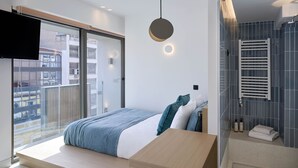 A modern bedroom with a large bed, a TV mounted on the wall, and a view of the outside balcony. - Twinn Downtown Piraeus (Piraeus)