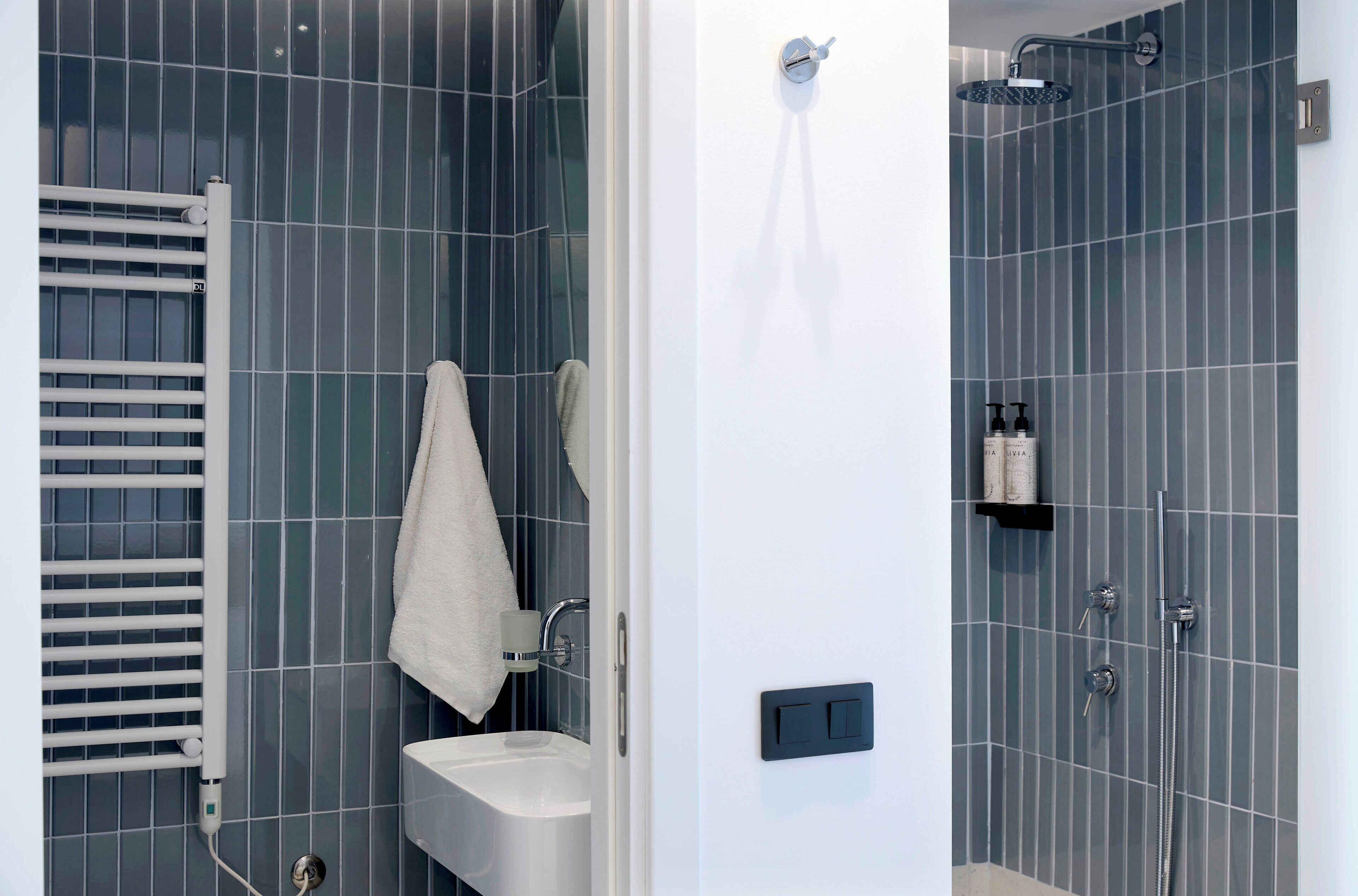 Un baño moderno con un lavamanos blanco, una toalla colgada en la pared y una zona de ducha con cabezal de ducha manual.