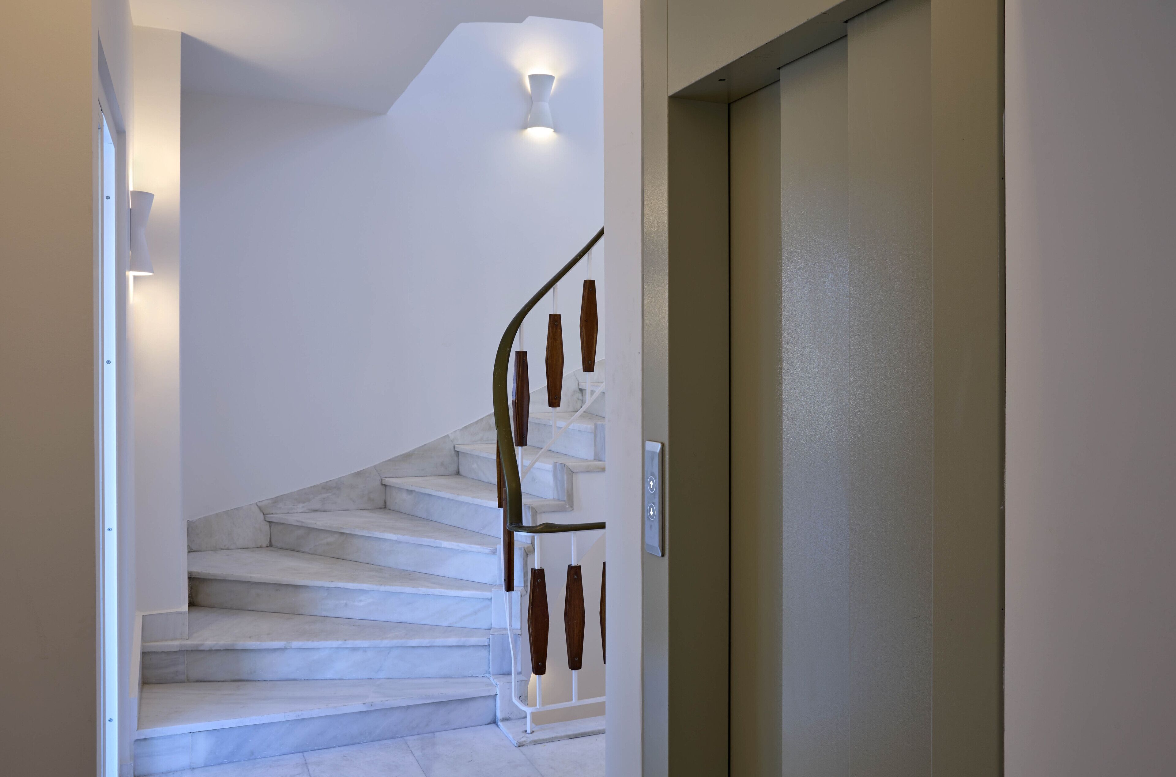 Una escalera con peldaños blancos y barandilla de madera, que lleva a una puerta con un interruptor de luz.