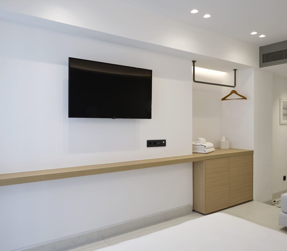 A modern bathroom with a large mirror, a mounted TV, and a wooden vanity.