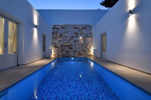A swimming pool with a stone wall and lighting on the sides. - Nisides Villas Naoussa (Naousa)