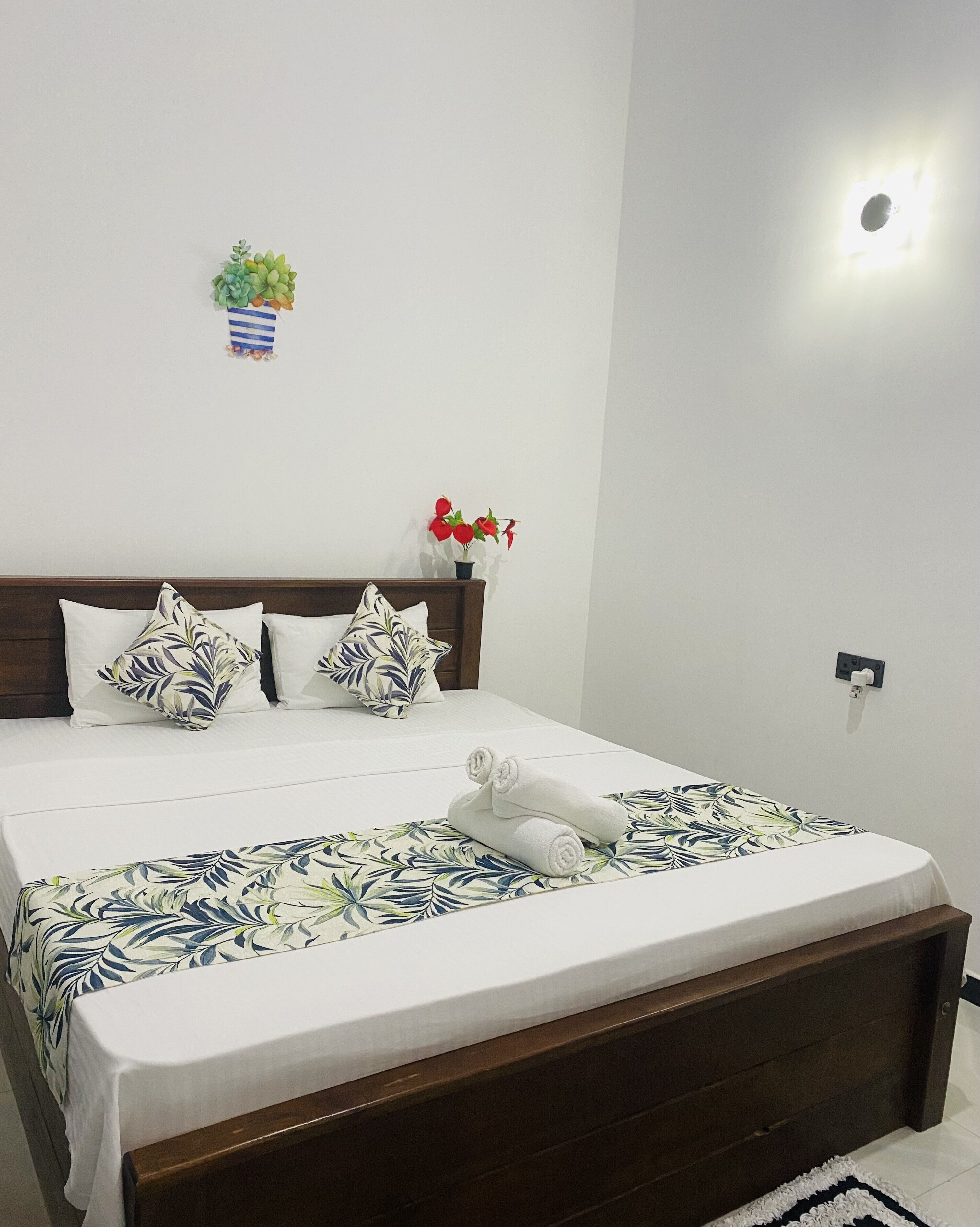 Una cama impecablemente vestida con una colcha de estampado floral, un cabecero de madera y dos almohadas con motivos de hojas.