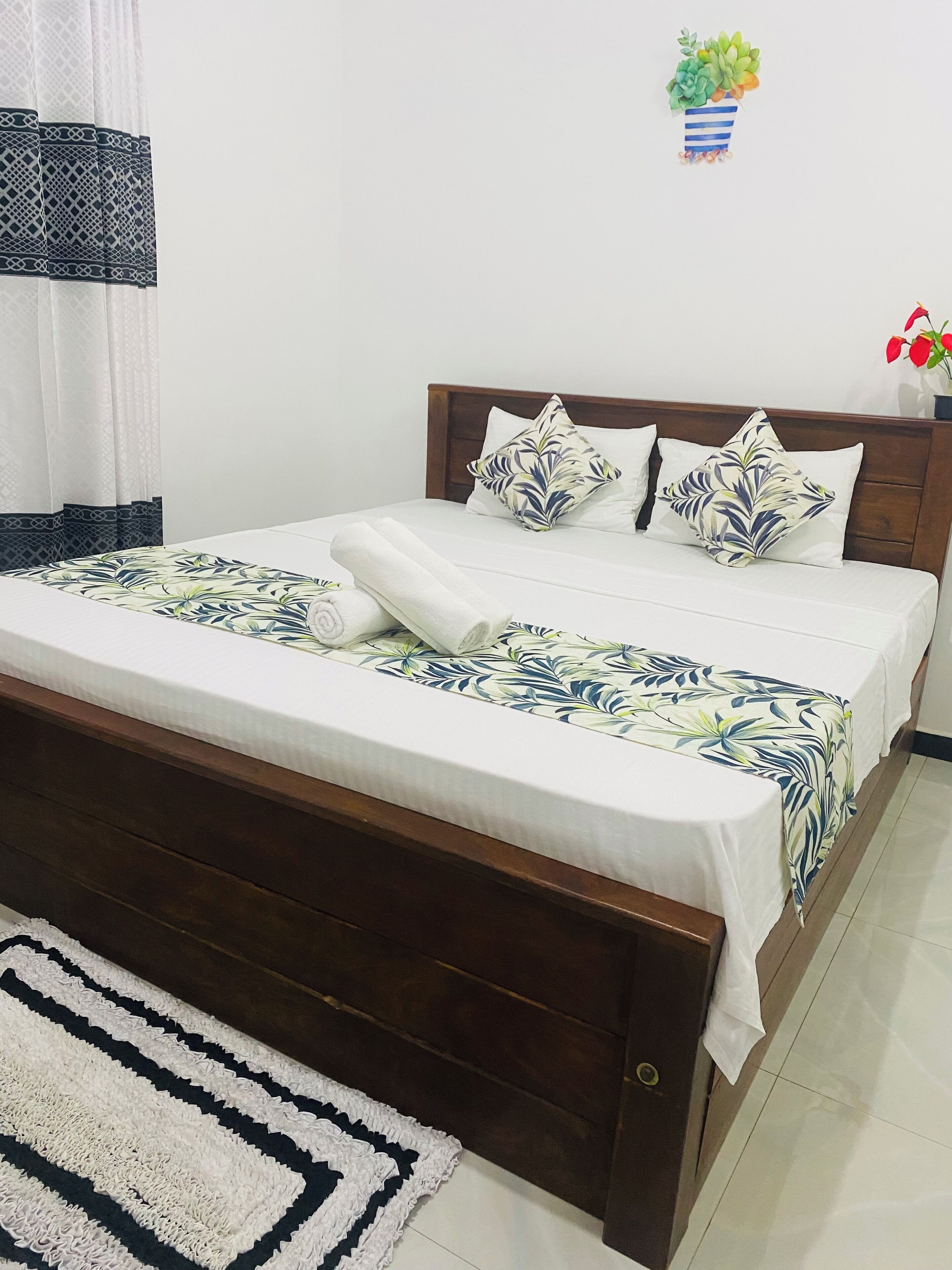 A neatly made bed with a floral-patterned bedspread, a wooden headboard, and a white pillow with a leaf design.