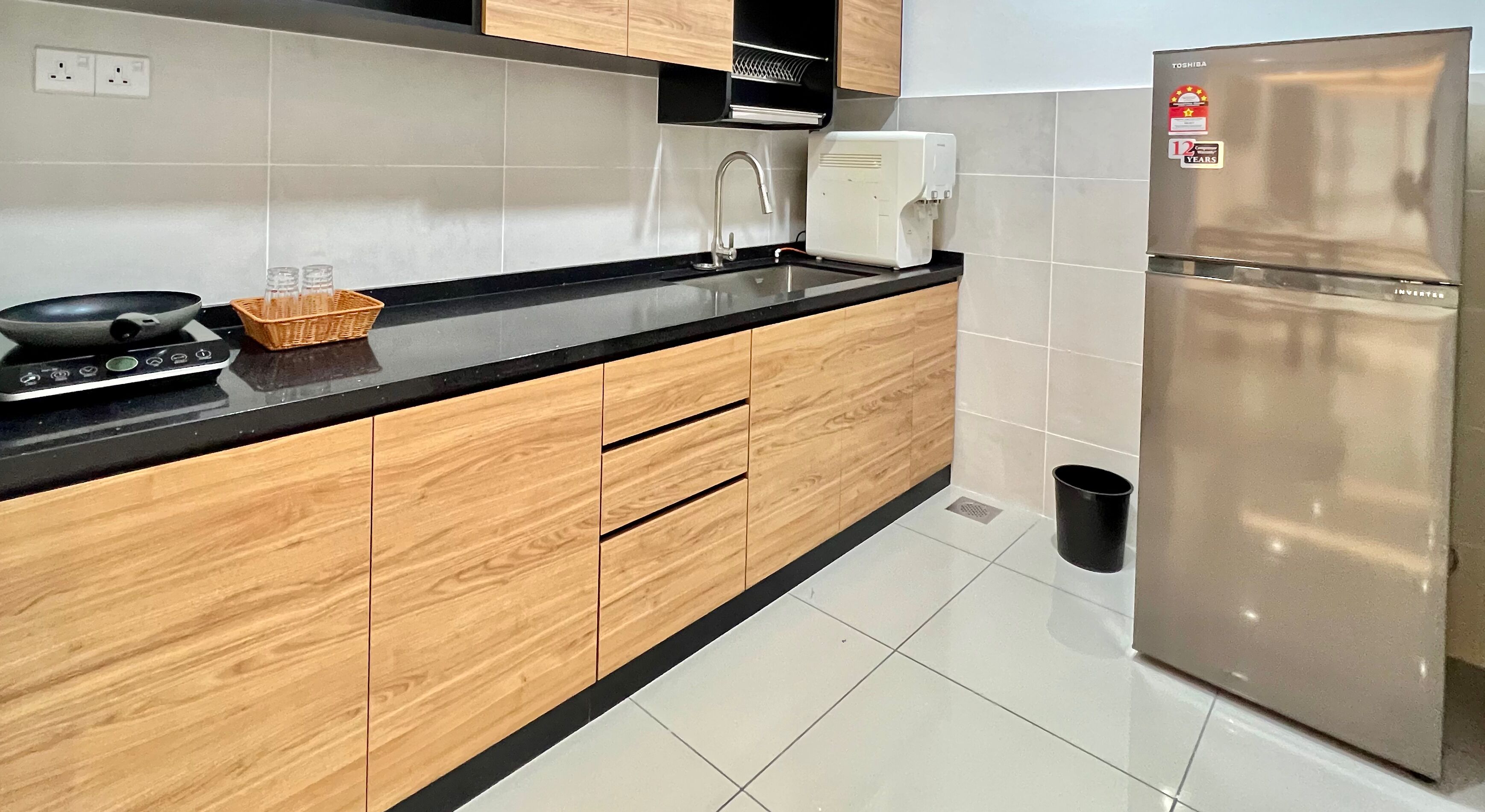 A modern kitchen with wooden cabinets, a stainless steel refrigerator, a black countertop, and a sink.