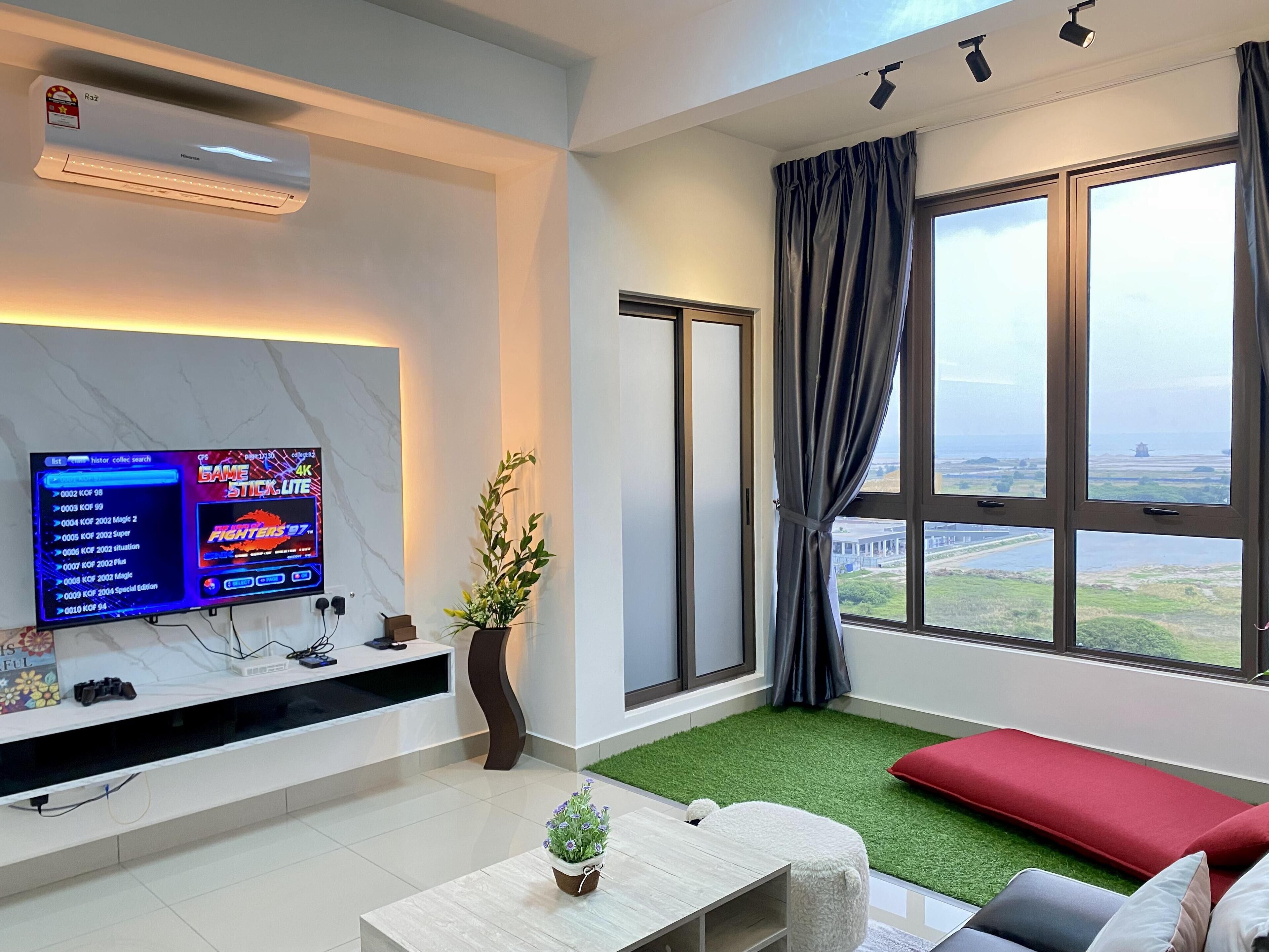 A modern living room with a flat-screen TV displaying a video game, a sofa, a coffee table, and a large window with a view of the landscape.
