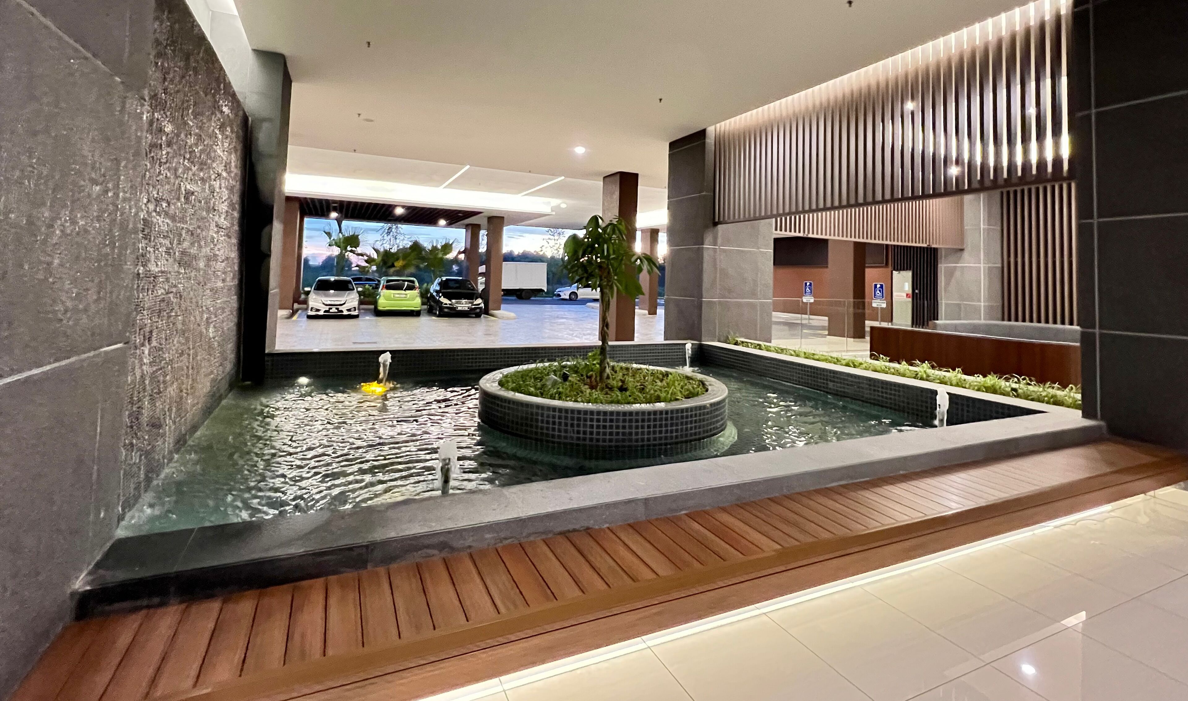 Un espace piscine intérieur moderne, doté d’un élément aquatique central, entouré d’une terrasse en bois et d’un sol carrelé.