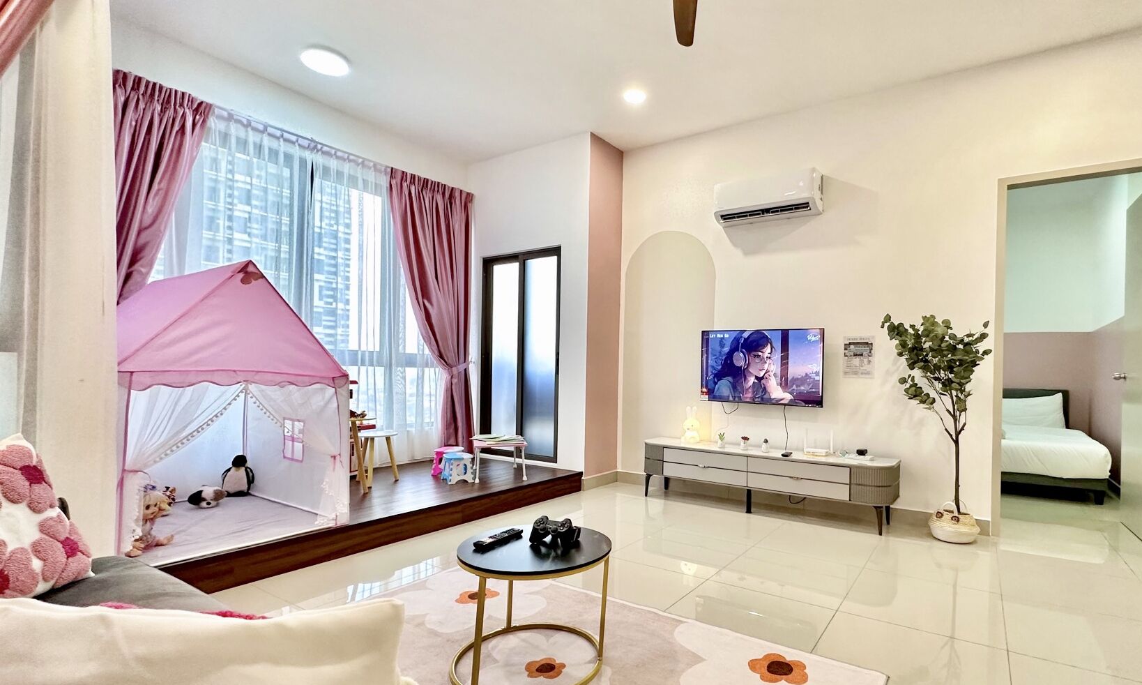 A modern hotel room with a pink play tent, a TV, a bed, and a small plant.